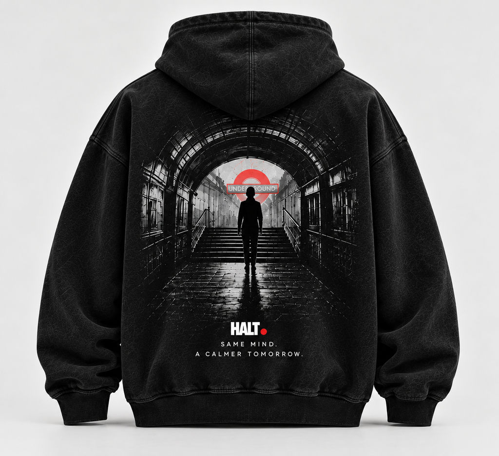 HALT. London Underground Hoodie in washed black, back view showing a silhouetted figure walking through a Tube tunnel toward a red roundel with SAME MIND. A CALMER TOMORROW. print