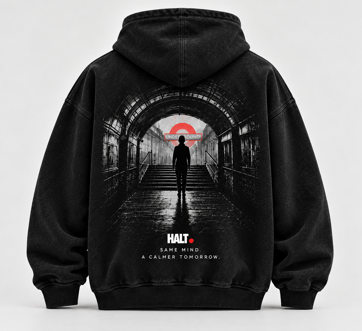 HALT. London Underground Hoodie in washed black, back view showing a silhouetted figure walking through a Tube tunnel toward a red roundel with SAME MIND. A CALMER TOMORROW. print